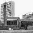 View from NNE showing chimney, NE block and part of central block of foundry with tower blocks under construction in background