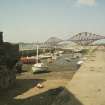 General view from SSW showing boats moored in harbour at low tide with Forth Bridge in background