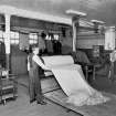 Scanned image of Peebles, Dean Park, Holland and Sherry's Cloth Warehouse
Dating from 1950s, copied by RCAHMS in 1996: interior view showing the Measuring and Folding Department, with two cloth folding machines in action