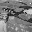 Oblique aerial view centred on the cropmarks of the roundhouses, souterrains, pits and rig at Hatton of Fintray with the village adjacent, looking to the NNW.