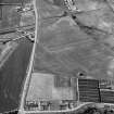 Oblique aerial view centred on the cropmarks of the ring ditch, pits and windmill at Sandend with Glenglassaugh Distillery adjacent, looking to the WNW.