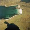 Oblique aerial view centred on the remains of the shieling huts and lazy-beds with the building and remains of the building and the remains of the fish trap adjacent, taken from the W.

