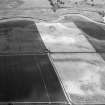 Oblique aerial view centred on the cropmarks of a palisaded enclosure, ring ditches, pits and rig at Suttie, looking to the SSE.