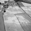 Oblique aerial view centred on the cropmarks of the enclosures, roundhouses, souterrain, pits and rig at Hatton of Fintray  with the village adjacent, looking to the NNW.