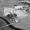 General oblique aerial view centred on the cropmarks of the barrow, enclosures, roundhouses, souterrain, pits and rig at Hatton of Fintray with the village adjacent, looking to the NNW.