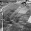 Oblique aerial view centred on the cropmarks of the roundhouses and ring ditches of the unenclosed settlement with the farmstead adjacent at Newbigging, looking to the NW.