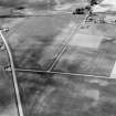 Oblique aerial view centred on the cropmarks of the roundhouses and ring ditches of the unenclosed settlement with the farmstead adjacent at Newbigging, looking to the NW.