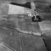 Oblique aerial view centred on the cropmarks of the roundhouses and ring ditches of the unenclosed settlement with the farmstead adjacent at Newbigging, looking to the NNW.