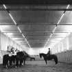 Interior view of Riding School (Block E) showing arena and regiment mounted on horses in foreground, Hyde Park Cavalry Barracks, London.
