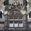 View of part of clocktower, above main door, showing two royal figures flanking a tympanum containing three putti.