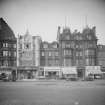 View from south of 100 - 103 Princes Street, Edinburgh, showing cars and shop fronts, including Drummond Young, E. Pass & Sons, J.B. Green & Sons Ltd, Boots Chemists, Durie Brown’s Ltd, Hector Powe, John Cotton Ltd Tobacco Manufacturers, Over-seas House, Birrel and Hope Brothers.