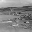 Maidens, general view, showing Maidens Harbour and Ardlochan Road. A large military shed, partially unroofed showing belfast roof trusses. A tram track leads from the building to the slip suggesting storage of equipment used at sea, possibly for target training. Oblique aerial photograph taken facing south-east.