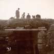 Photograph of part of a Broch showing five men, props, grass and stones