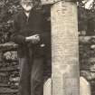 Scanned image of photograph of John Nicolson beside carved headstone with names and dates of the dead on it