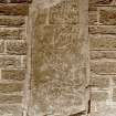 Scanned image of photograph of Pictish symbol stone, which is decorated with two rectangles, a bird , a fish, ogham writing,  and horsemen. There is a wall directly behind the stone