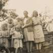 Scanned image of photograph of Jean Hughes and Mrs R Begg with five female children standing beside a wall with a female statue sat on the wall to the right (see J 8939 PO)