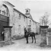 View of the south front of the stables with a figure of horseback in the foreground and another at the stable door.