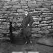A figure, probably Henry M Macleod, Clerk of Works, standing in front of the outer face of the blockhouse of Clickimin broch, Lerwick.