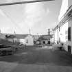 Bowmore Distillery
General view from SE within W yard of the distillery, showing SW end of floor maltings (right), still house (centre), and offices (left), with bonded warehouse block in the background