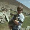 A Soay sheep in the arms of Alan Leith, RCAHMS, Village Bay.