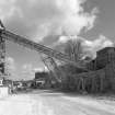 View from W showing overhead conveyor from primary crusher (base visible to right) to former shaft kilns (now storage hoppers to left).  The supporting strut for the conveyor is a surviving portion of one of the original conveyors supplying the shaft kilns