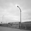 View of nearby concrete bus shelter and lamp standard from SE.