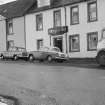View of the Crown Inn, 36 Main Street, Glenluce from south west, showing James Muir's premises and cars and lorry.