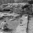 Excavation photograph : general view of ruins, rock face, and people working, looking west.