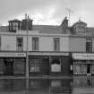 View of 41-47 Princes Street, Ardrossan, from SW, showing the premises of James R MacGregor chemist and druggist, an optician, a hairdresser and Cockburns dispensing chemist.