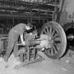 Glasgow, Springburn, St Rollox Locomotive Works, interior.
View of man removing a crane from a steam engine wheel.