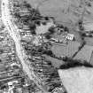 Oblique aerial view centred on the remains of the priory and burial ground with the church and village adjacent, taken from the NE.