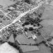 Oblique aerial view centred on the remains of the priory and burial ground with the church and village adjacent, taken from the NNW.