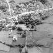 Oblique aerial view centred on the remains of the priory and burial ground with the church and village adjacent, taken from the NW.