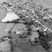 Oblique aerial view centred on the remains of the priory and burial ground with the church and village adjacent, taken from the SW.