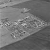 Oblique aerial view of Crail Airfield centred on the remains of buildings, a water tank and a hut, taken from the NNW.