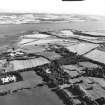 General oblique aerial view looking across the airfield, aircraft hangers, buildings and oil pipeline construction towards the Black Isle, taken from the N.