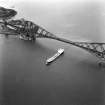 Aerial view from the South West showing a cargo ship passing underneath the bridge.
