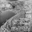 Oblique aerial view looking across the oil fuel depots, the military training camp and farmsteading towards the village, taken from the SSE.