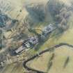 Oblique aerial view centred on the country house with stables and bridge adjacent, taken from the NNE.