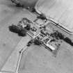 Oblique aerial view centred on the church and burial ground with manse, schoolhouse, farmsteading and road bridge adjacent, taken from the WNW.