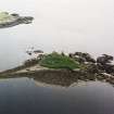 Oblique aerial view centred on the remains of the broch with the ruin of the building adjacent, taken from the NNE.