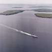 General oblique aerial view looking across a frigate in the Sound of Hoxa, towards South Ronaldsay and Mainland, taken from the SSW.