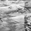 Corrymuckloch, oblique aerial view, taken from the ESE, showing the Crieff to Dalnacardoch military road running across the centre of the photograph. An area of hut-circles, clearance cairns and field banks is visible in the centre. A hoard find spot, in peat cuttings, is visible as a dark patch in the centre left of the photograph.