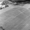 Oblique aerial view centred on the faint cropmarks of an enclosure with quarry, Roman Road and linear cropmarks adjacent, taken from the SE.