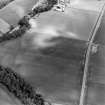 Oblique aerial view centred on cropmarks of an enclosure, with a Roman road adjacent, taken from the W.