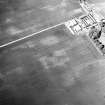 Newbigging, oblique aerial view, taken from the SSE, centred on the cropmarks of an enclosure, pits and an unenclosed settlement. The cropmark of a barrow is visible in the left centre half of the photograph.