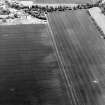 Oblique aerial view centred on the cropmarks of the ring-ditch and possible unenclosed settlement with the cropmarks of the palisaded enclosure and rig adjacent, taken from the ENE.