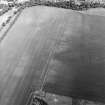 Oblique aerial view centred on the cropmarks of the ring-ditch and possible unenclosed settlement with the cropmarks of the palisaded enclosure and rig adjacent, taken from the WSW.