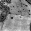 Oblique aerial view from the WSW, centred on the cropmarks of an enclosure. Chapel on Leader Country House is visible in the top left-hand corner of the photograph.