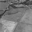 Oblique aerial photograph of Glenluce taken from the SSE, centred on the cropmarks of a Roman temporary camp.